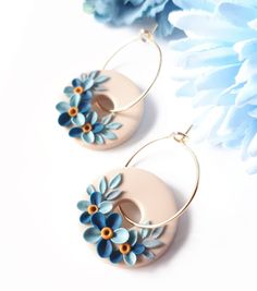 a pair of earrings with blue flowers on them next to a flowery planter