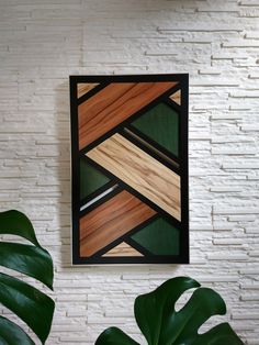 a white brick wall with a green plant in front of it and a wooden framed artwork hanging on the wall