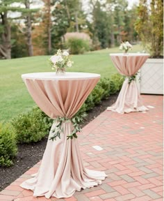 two tables covered in pink cloths with flowers on each table and greenery at the top