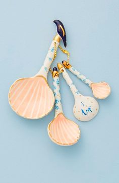 three ceramic spoons with shells attached to them on a blue background, hanging from a gold - plated chain