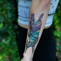 a woman with a tattoo on her arm holding a purple flower in her left hand