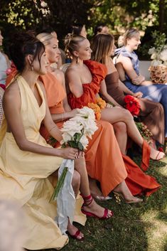 a group of women sitting next to each other on top of a grass covered field