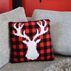 a red and black plaid pillow with a deer head on it, sitting on a couch