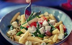 a person is holding a fork over a pasta salad