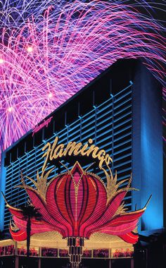 fireworks light up the night sky in front of a building with an advertisement on it