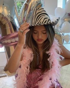 a woman wearing a zebra print hat and pink feather boa around her neck with balloons in the background