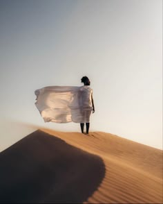 a woman standing on top of a sand dune holding a white cloth in her hand