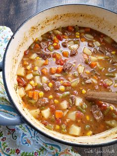 a pot filled with stew and vegetables on top of a wooden table next to a spoon