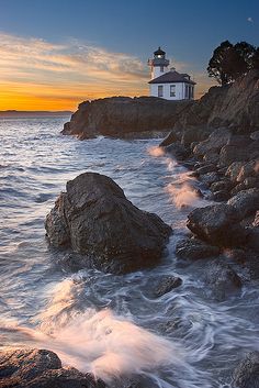 a lighthouse on top of a rocky cliff next to the ocean with waves coming in