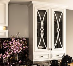 an elegant kitchen with white cabinets and marble counter tops, along with a vase filled with pink flowers