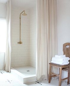 a white bathroom with black and white tile flooring, shower curtain, and wooden chair