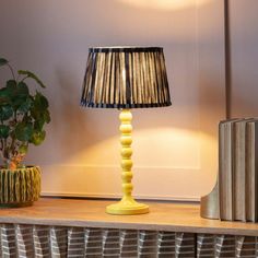 a lamp on a table next to a book and a potted plant in a corner