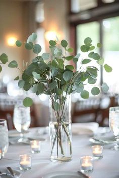 a vase filled with greenery sitting on top of a table next to silverware