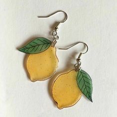 two yellow lemons with green leaves are hanging from silver earwires on a white surface