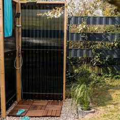 an outdoor shower in the middle of a garden with gravel and grass around it, next to a wooden fence