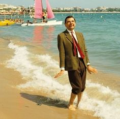 a man in a suit and tie standing on the beach with his hands out to the water