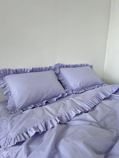 a bed with purple ruffled sheets and pillows