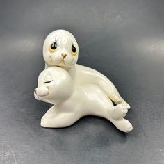 a white ceramic cat sitting on top of a kitten figurine with yellow eyes