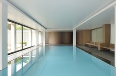 an indoor swimming pool with blue water and wooden benches on either side, surrounded by windows