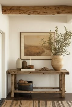 a wooden table topped with a vase filled with flowers next to a painting on the wall