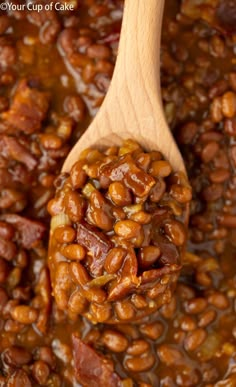 a wooden spoon filled with baked beans and sauce on top of a pan full of cooked beans