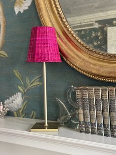 a pink lamp sitting on top of a white shelf next to a mirror and books