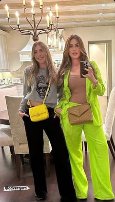 two women standing next to each other in front of a chandelier holding cell phones