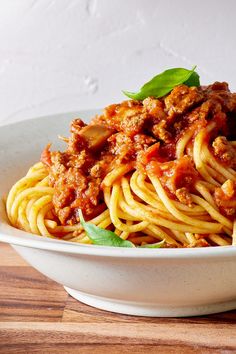 a white bowl filled with spaghetti and meat sauce on top of a wooden cutting board