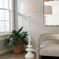 a white floor lamp next to a potted plant in a living room with a mirror on the wall