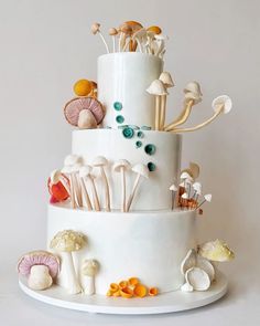 a three tiered white cake with mushrooms on the top and sides, surrounded by other edible items