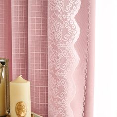 a candle is sitting on a table next to a window with pink curtains and lace