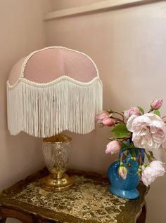 a blue vase with pink flowers on a table next to a lamp and other items