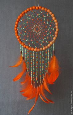 an orange beaded dream catcher with feathers hanging from it's side on a gray background