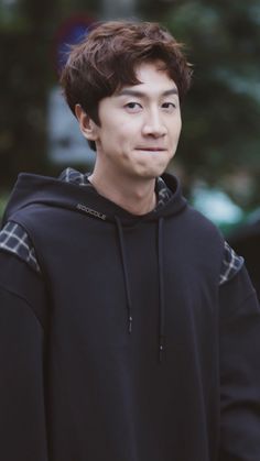 a young man wearing a black hoodie standing in front of a tree and looking at the camera