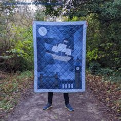 a person holding up a blue quilt with a boat on it in front of some trees