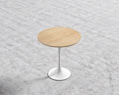 a small round table with a wooden top on the concrete floor, next to a chair