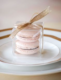 three macaroons in a clear box on a white plate with a gold ribbon