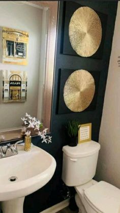 a white toilet sitting next to a sink in a bathroom under two gold circles on the wall