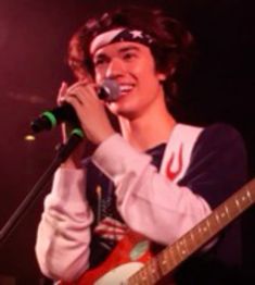 a young man singing into a microphone and holding a guitar in front of his face