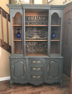 an old china cabinet painted with chalk paint and gold lettering on the doors, in front of stairs