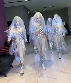 several people dressed in silver and white walking down a hall with lights on their bodies