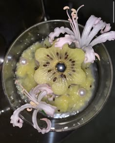 a glass bowl filled with fruit and flowers on top of a black countertop next to a sink