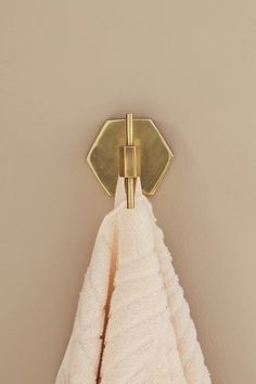 a white towel hanging from a gold hook on a beige wall with a brown background