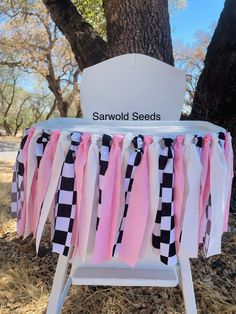 a white chair sitting under a tree with pink and black ribbons