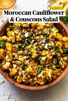 a wooden bowl filled with roasted cauliflower and green beans next to lemon wedges