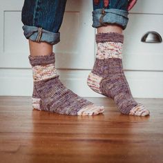 a person standing on a wooden floor with their feet up and wearing socks that are knitted in different colors