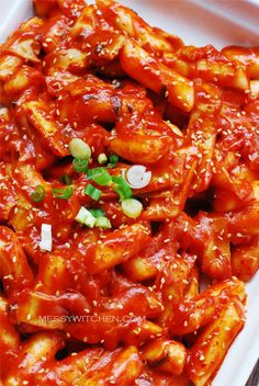 chicken wings covered in marinara sauce on a white platter with green onions and scallions