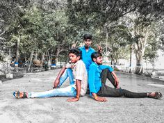 three young men sitting on the ground in front of trees