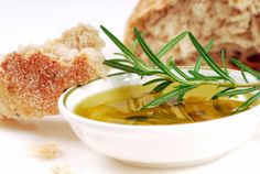 a white bowl filled with green liquid next to bread and sprig of rosemary