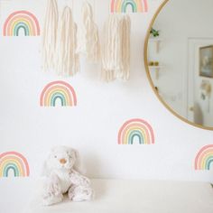 a white teddy bear sitting on top of a bed next to a wall with rainbows